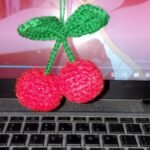 Red crochet cherry charm with green stems and leaves