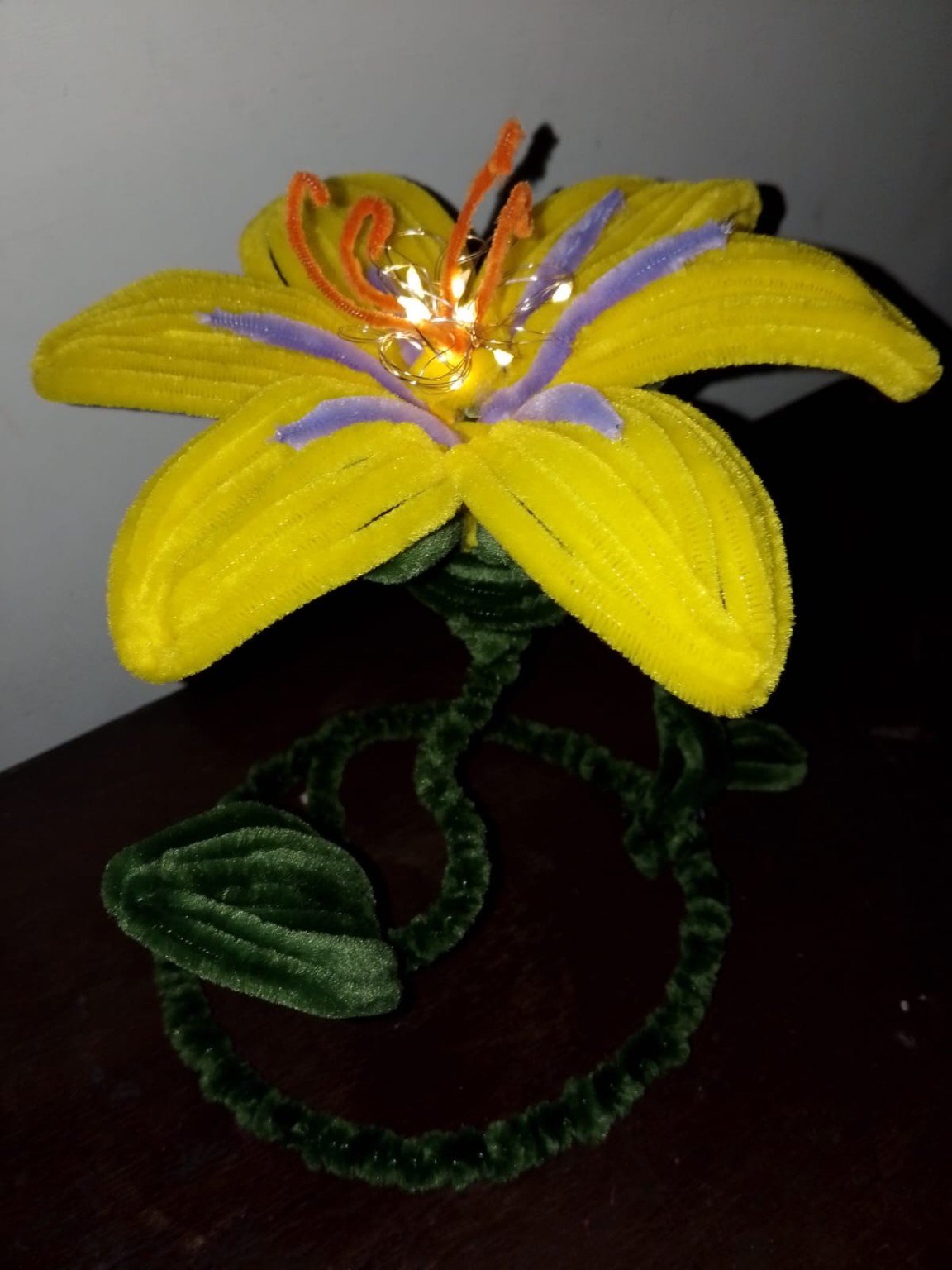 Yellow crochet lily flower lamp with green leaves and a round base